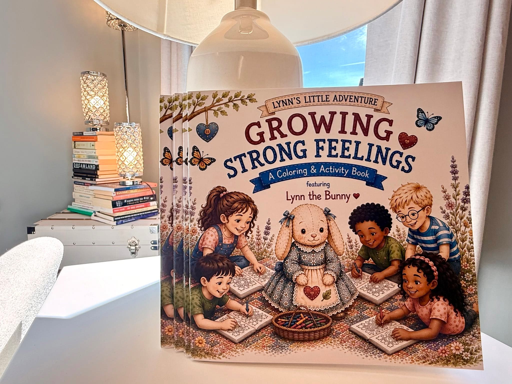 Cover of Growing Strong Feelings, a coloring and activity book featuring Lynn the Bunny. Lynn, a stitched ragdoll bunny in a blue flowered dress, sits on a quilt with five children who are coloring.